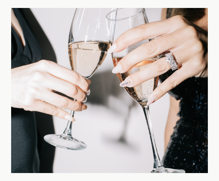 Two women clink champagne glasses together, celebrating a joyful moment with smiles and elegance.