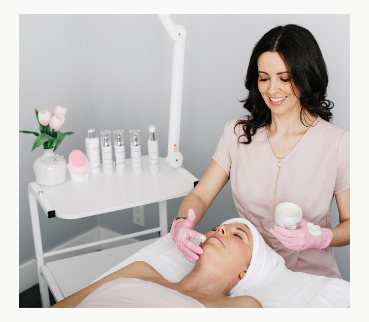 A woman receiving a facial treatment, relaxing as a professional applies skincare products to her face and body.